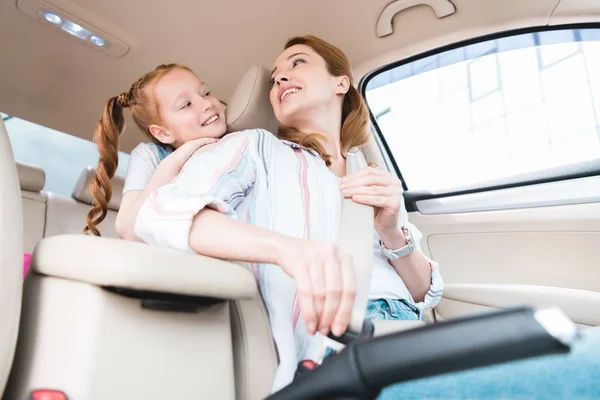 Low angle view of woman fastening seat belt while driving car with daughter behind — Stock Photo