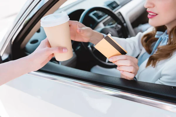 Empresária com cartão de crédito na mão tomando café para ir enquanto sentado no carro — Fotografia de Stock