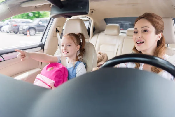 Porträt einer lächelnden Mutter, die Auto fährt und ihre Tochter in der Nähe wegzeigt — Stockfoto