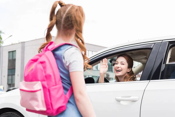 Foco seletivo de mulher sorridente no carro acenando para filha com mochila — Fotografia de Stock