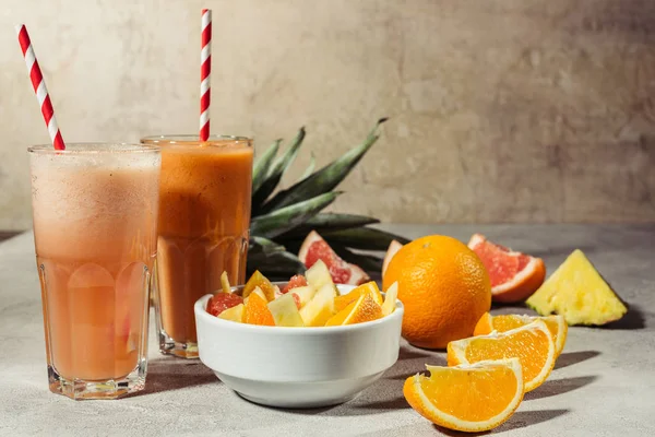Очки с цитрусовыми соками и фруктами на сером столе — стоковое фото