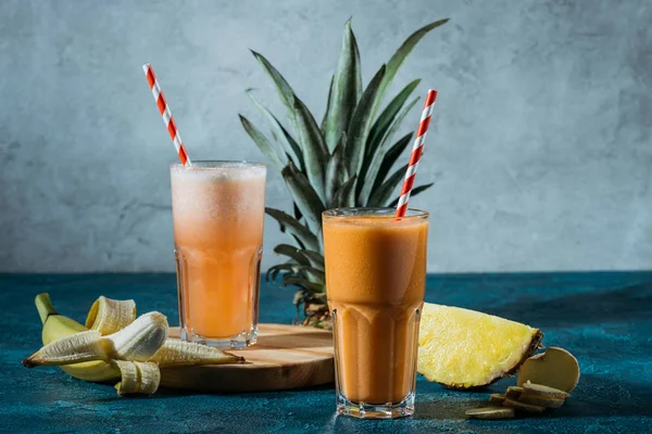 Healthy fruit juice in glasses by tropical fruits on table — Stock Photo