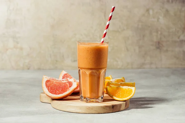 Sumo fresco em vidro com pedaços de laranja e toranja em tábua de madeira — Fotografia de Stock