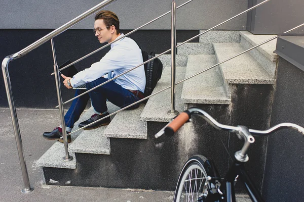 Side view of young man in eyeglasses sitting on stairs and using laptop — Stock Photo