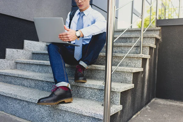 Recortado disparo de joven empresario sentado en las escaleras y el uso de la computadora portátil - foto de stock