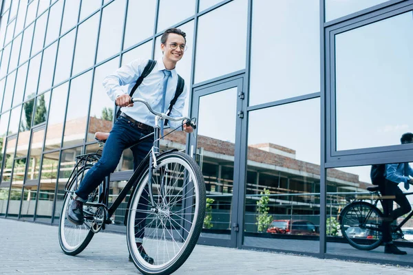 Beau jeune homme souriant en lunettes et vêtements formels vélo d'équitation sur la rue — Photo de stock