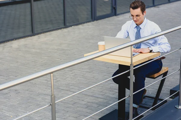 Hochwinkelaufnahme eines hübschen jungen Geschäftsmannes in Brille mit Laptop, während er draußen sitzt — Stockfoto