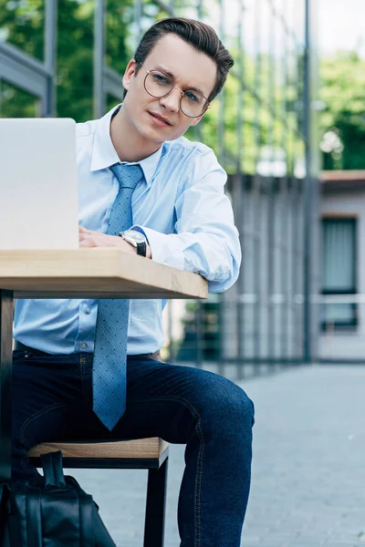 Beau jeune homme d'affaires dans les lunettes à l'aide d'un ordinateur portable et regardant loin à l'extérieur — Photo de stock