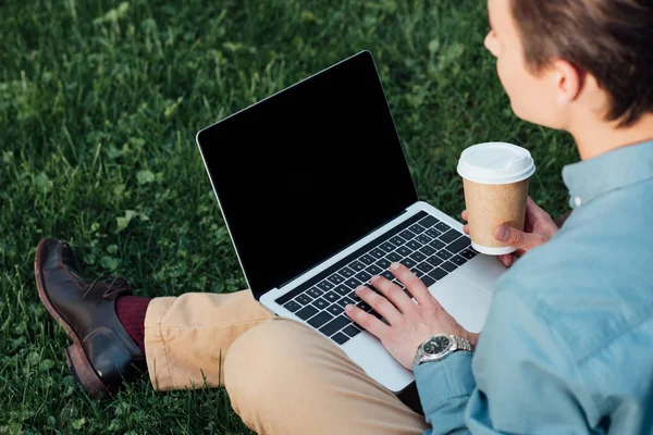 Tiro recortado de freelancer beber café e usando laptop na grama — Fotografia de Stock