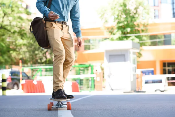 Cropped shot of young man using smartphone and riding skateboard on street — Stock Photo