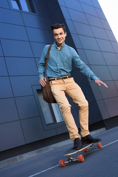 Beau jeune homme souriant chevauchant skateboard sur la rue — Photo de stock