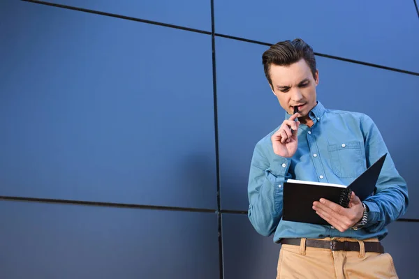 Schöner nachdenklicher junger Mann mit Notizbuch und Stift — Stockfoto