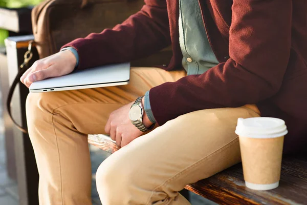 Cropped shot of man holding laptop and sitting on bench — Stock Photo