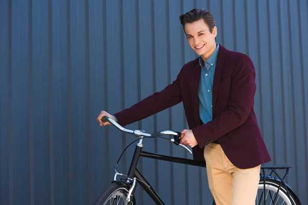 Beau jeune homme debout avec vélo et souriant à la caméra — Stock Photo