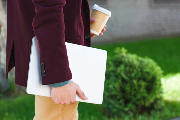 Cropped shot of man holding laptop and coffee to go on street — Stock Photo
