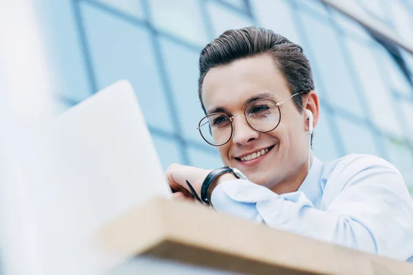 Bell'uomo d'affari sorridente in occhiali usando il computer portatile fuori, messa a fuoco selettiva — Foto stock