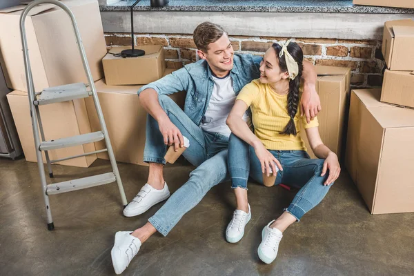 Beautiful young couple with paper cups sitting on floor while moving into new home — Stock Photo