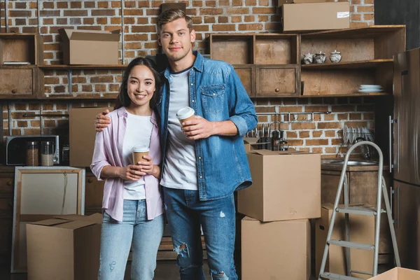 Junges gemischtrassiges Paar mit Pappbechern Kaffee umarmt sich in der Küche beim Einzug in ein neues Zuhause — Stockfoto