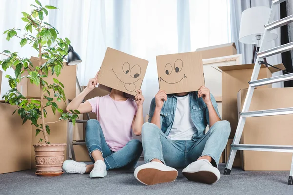 Pareja sentada en el suelo después de mudarse a un nuevo hogar con cajas en las cabezas - foto de stock