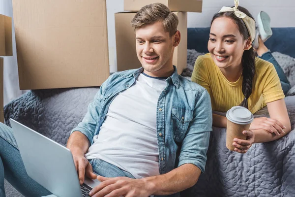 Hermosa pareja joven utilizando el ordenador portátil en el nuevo hogar después de la reubicación - foto de stock