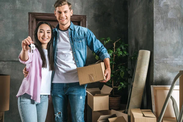 Glückliches junges Paar mit Kisten und Schlüssel zieht in neues Zuhause ein — Stockfoto