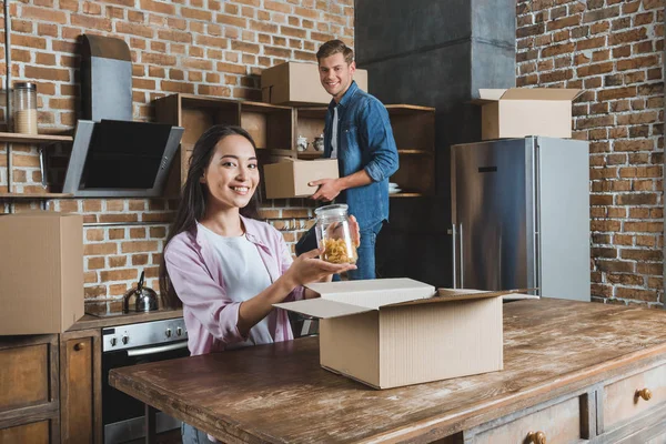 Hermosa pareja joven desempacando cajas en la cocina mientras se muda a un nuevo hogar - foto de stock