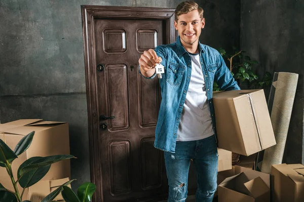 Attraktiver lächelnder Mann mit Schachtel und Schlüssel bezieht neues Zuhause — Stockfoto