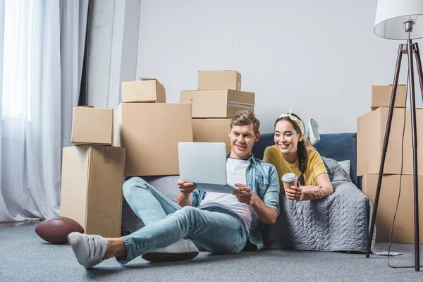 Beau jeune couple en utilisant un ordinateur portable tout en étant assis sur le sol à la nouvelle maison — Photo de stock