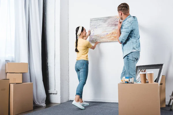 Young couple handing abstract picture on wall while moving into new home — Stock Photo