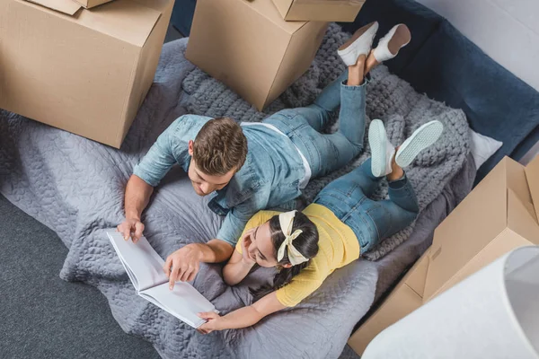 Blick aus der Vogelperspektive auf ein glückliches junges Paar mit Album, das sich nach dem Einzug in sein neues Zuhause im Bett entspannt — Stockfoto