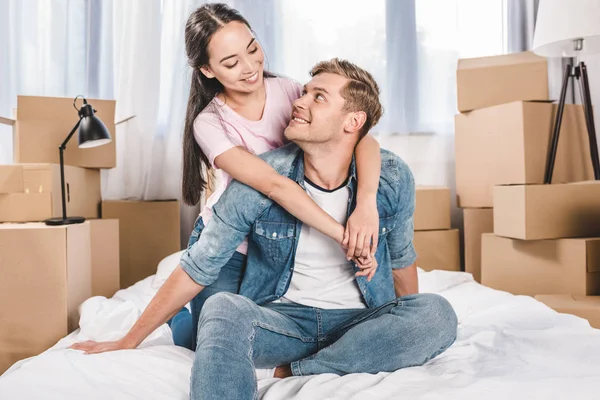 Feliz joven pareja sentada en la cama después de mudarse a un nuevo hogar - foto de stock