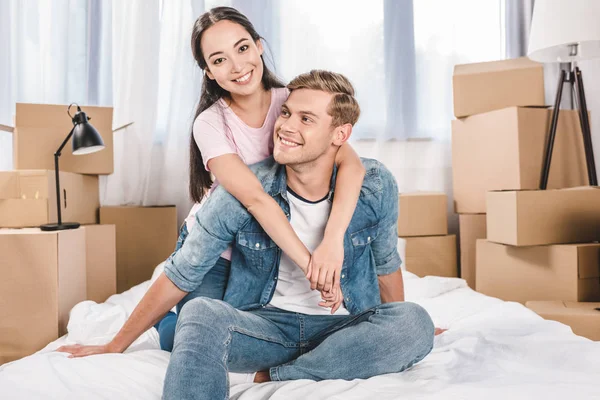 Belo jovem casal sentado na cama depois de se mudar para uma nova casa — Fotografia de Stock