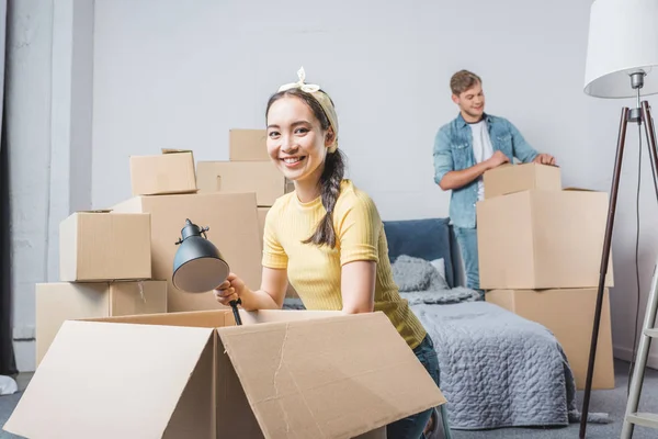 Feliz pareja joven desempacando cajas mientras se muda a un nuevo hogar - foto de stock