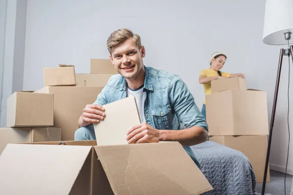 Belo casal jovem desempacotando caixas enquanto se move para nova casa — Fotografia de Stock