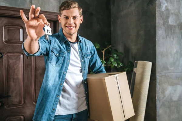 Bel homme souriant avec boîte et clé déménageant dans une nouvelle maison — Photo de stock