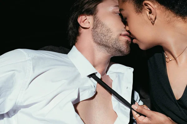 Jovem casal sexy multirracial em roupas pretas beijando no fundo escuro — Fotografia de Stock