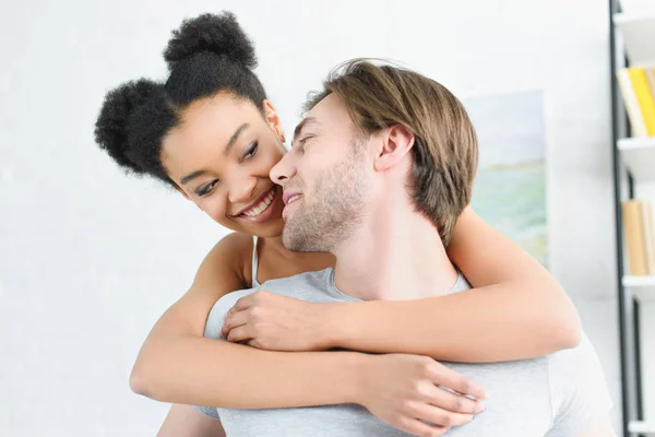 Retrato de la mujer afroamericana feliz abrazando novio en casa - foto de stock