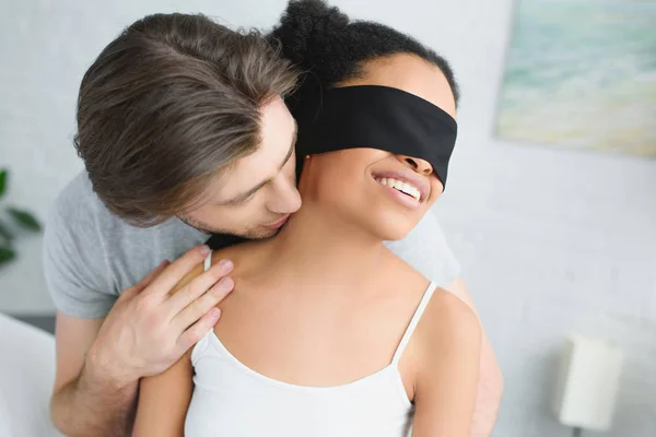Ritratto di uomo che abbraccia la fidanzata afro-americana con gli occhi coperti di panno nero a casa — Foto stock