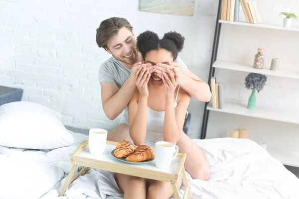 Multiracial young couple having breakfast in bed in morning at home — Stock Photo