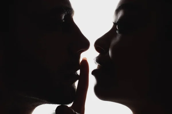 Vista lateral de silueta de mujer afroamericana mostrando señal de silencio a novio - foto de stock