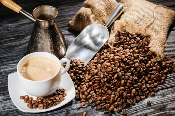 Vue grand angle de tasse à café avec cuillère et cezve sur tas de grains de café et sur table en bois rustique — Photo de stock