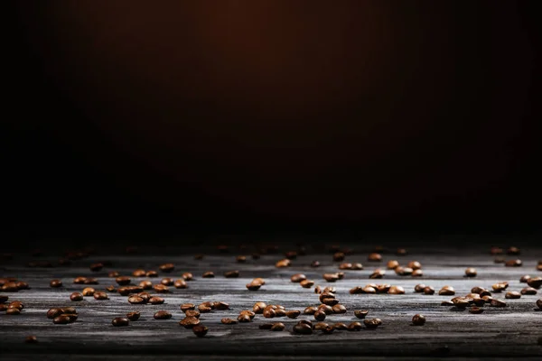 Rustic wooden table spilled with coffee beans on black — Stock Photo