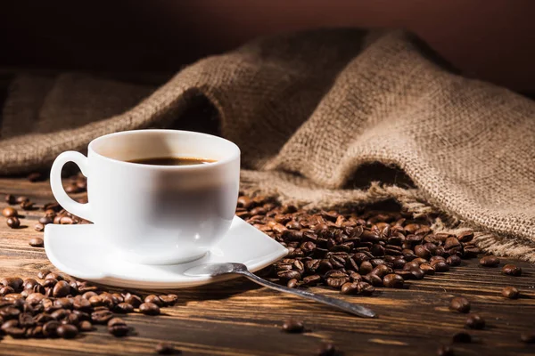 Чашка кави зі смаженою квасолею та мішковиною на дерев'яному столі — стокове фото