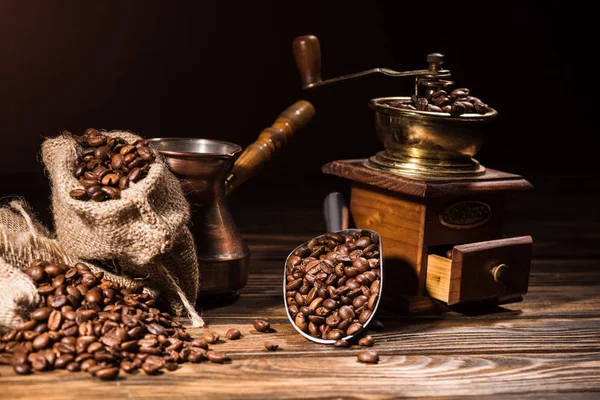 Metal scoop, vintage cezve and coffee grinder on rustic wooden table spilled with roasted beans — Stock Photo