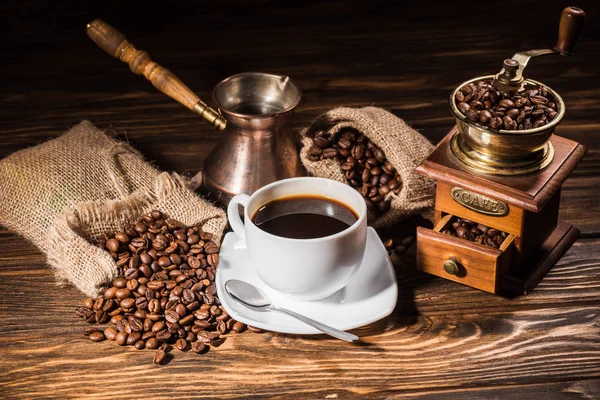 High angle view of coffee cup with vintage cezve and coffee grinder on rustic wooden table spilled with roasted beans — Stock Photo