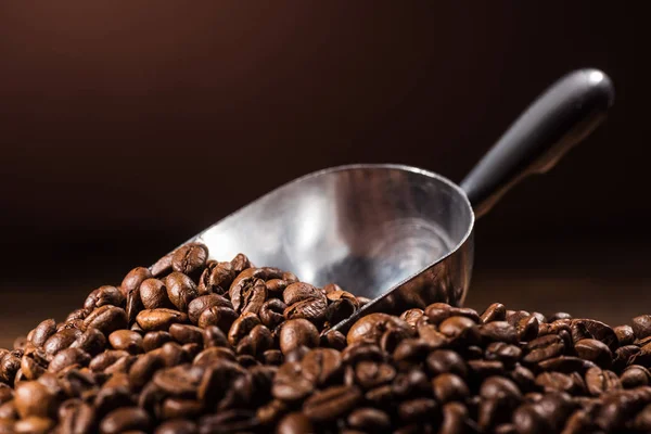 Close-up tiro de montão de grãos de café torrados com colher em fundo marrom escuro — Fotografia de Stock