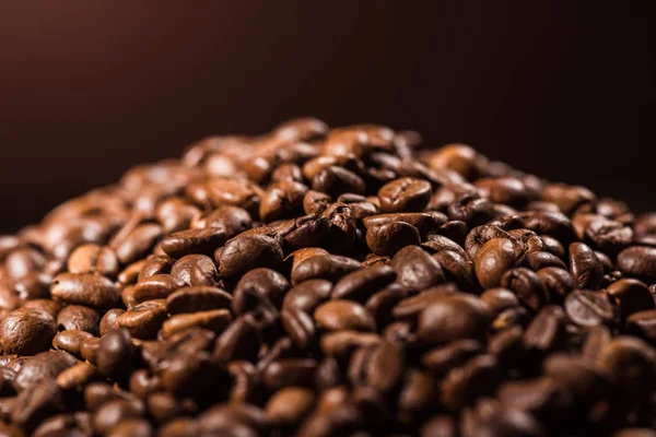 Primer plano de montón de granos de café tostados sobre fondo marrón oscuro - foto de stock