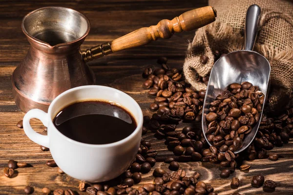 Close-up shot of cup of coffee with roasted beans and cezve — Stock Photo