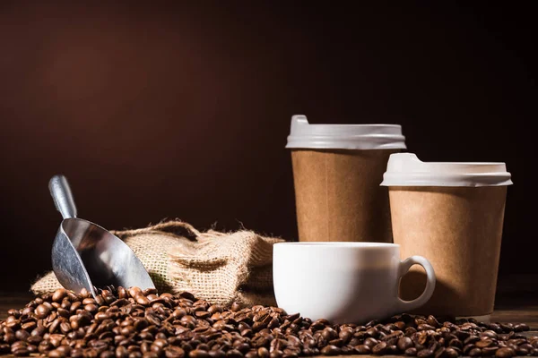 Крупный план куча кофейных зерен с бумажными чашками, совок и кружка на деревенском деревянном столе — стоковое фото