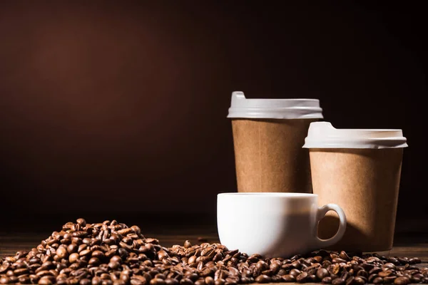 Nahaufnahme Haufen Kaffeebohnen mit Pappbechern und Becher auf rustikalem Holztisch — Stockfoto